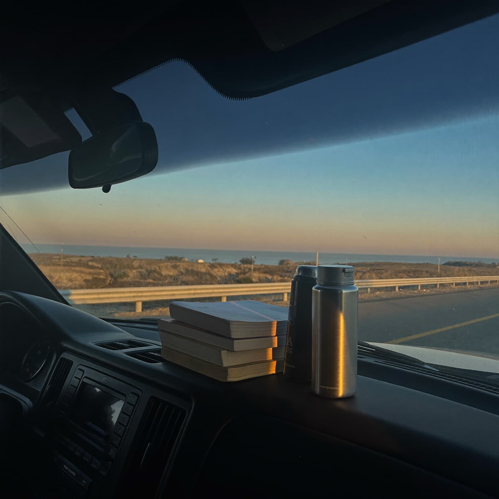 Logbooks and a thermos on a truck dashboard at dawn