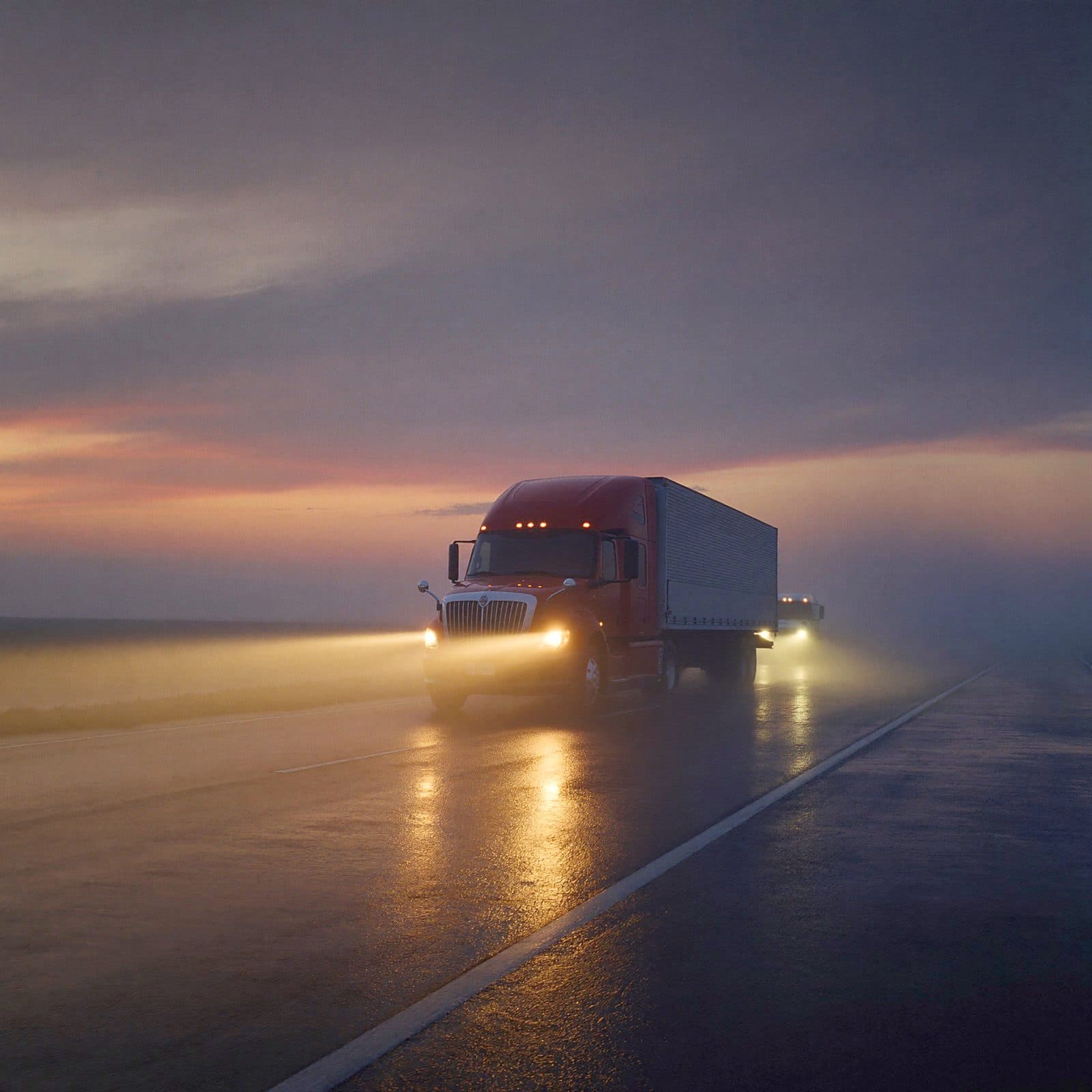 Semi-truck headlights cutting through rain and mist at dusk